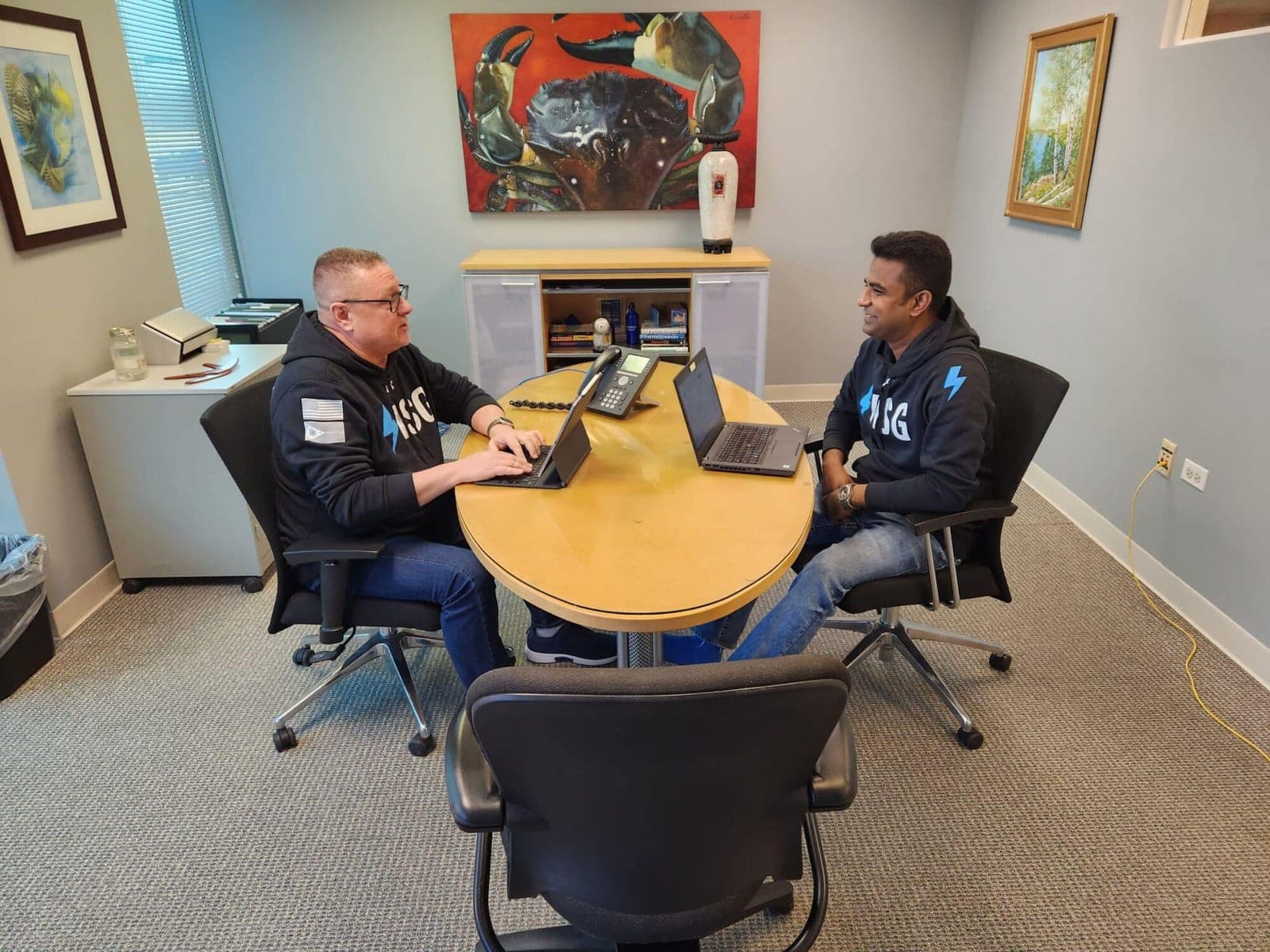 Two ISG teammates in branded hoodies working on laptops at a round office table